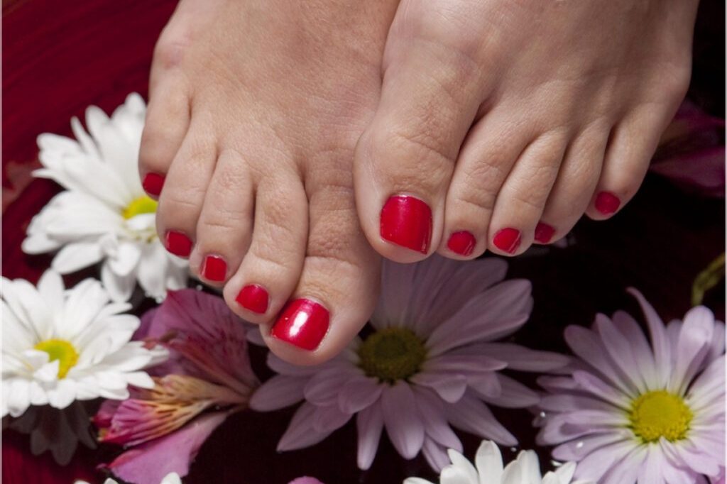Freshly painted red toenails in a flower foot soak